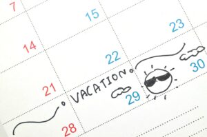 A calendar marked with the word 'VACATION' and a drawing of a sun wearing sunglasses. Paid time off for vacation provides employees with a structured opportunity to relax, recharge, and maintain a healthy work-life balance.